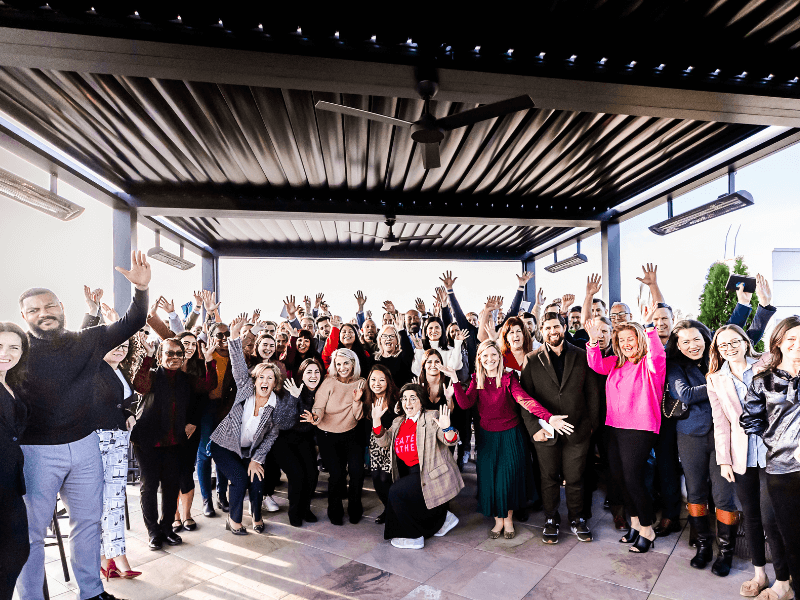 The Significance team cheering at the camera, all grouped under an outdoor pavilion together