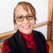 A woman with glasses in a red patterned turtleneck and black vest smiling at the camera